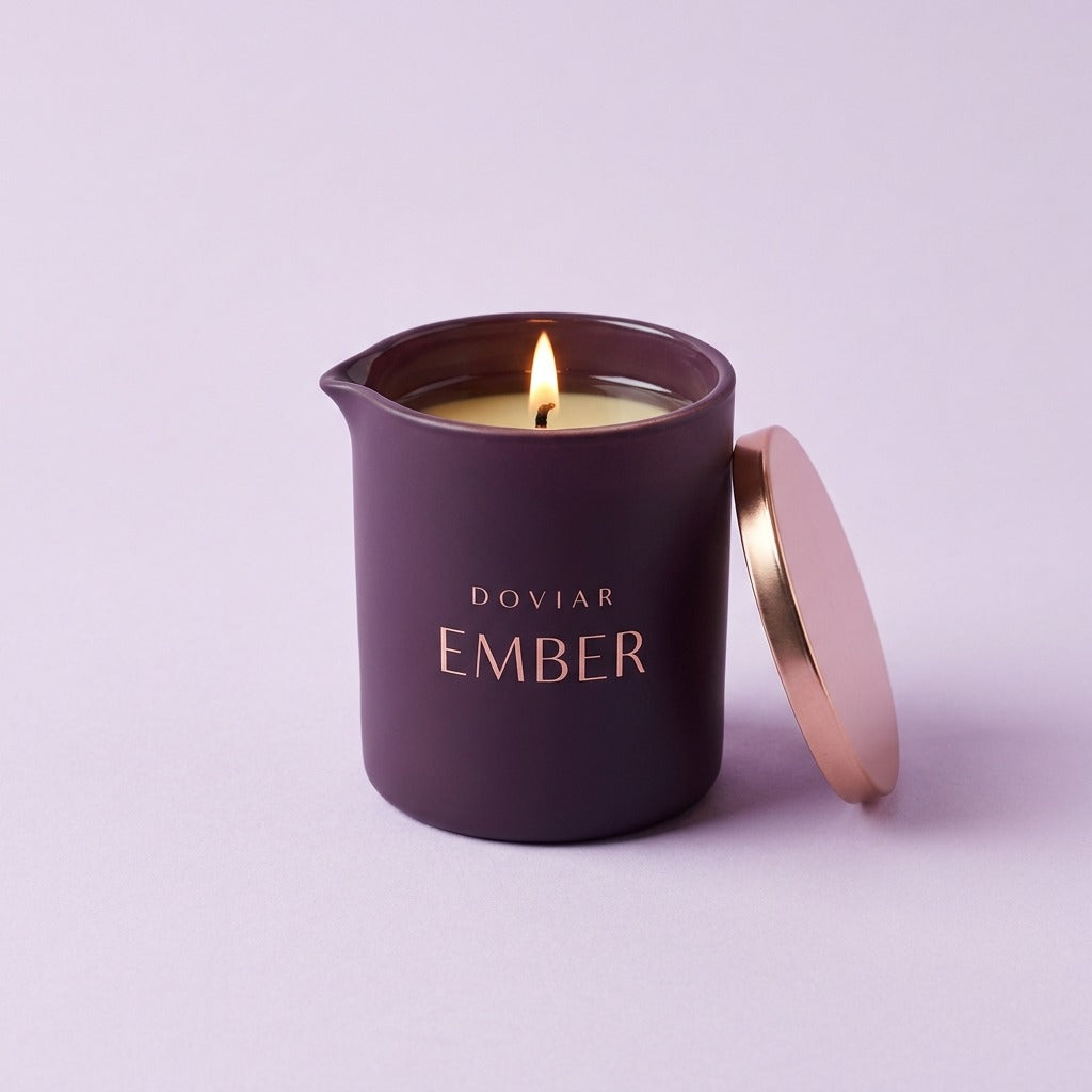 DOVIAR EMBER massage candle, lit, in a deep plum jar with a rose-gold lid